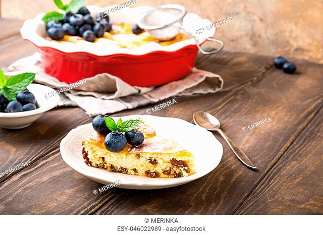 Piece of homemade cheesecake made from cottage cheese, decorated with blueberries and mint on wooden background. Healthy food concept with copy space