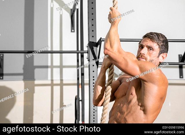 Fitness man doing rope climb exercise in gym. High quality photo
