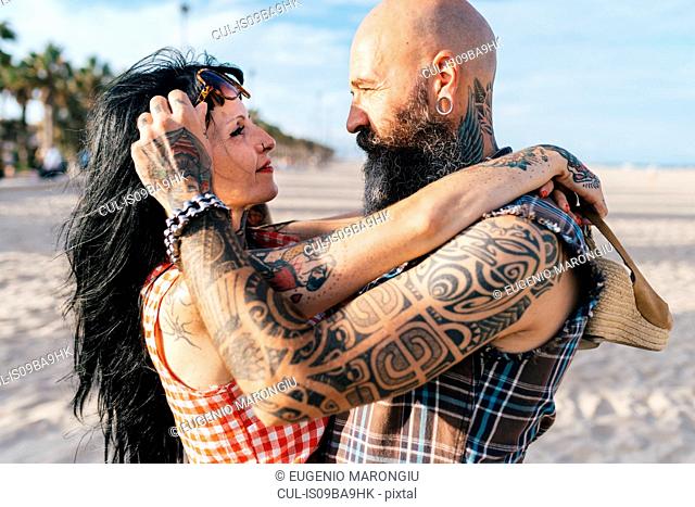 Mature tattooed hipster couple face to face on beach, Valencia, Spain