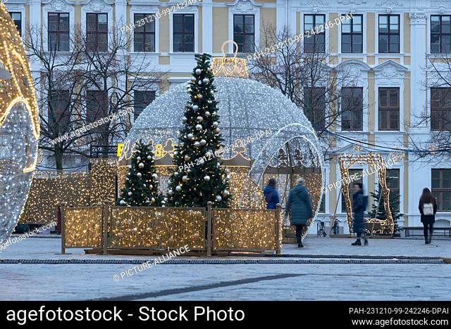 07 December 2023, Magdeburg: Passers-by walk across the cathedral square with the Christmas sculptures of the Magdeburg World of Lights in rainy weather