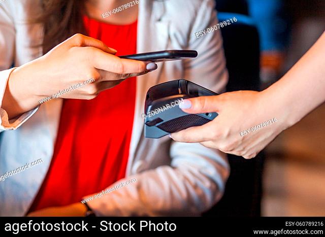 Closeup portrait of young woman sitting with mobile smart phone and paying by pay pass pos. contactless, nfc technology on cellphone and payment concept