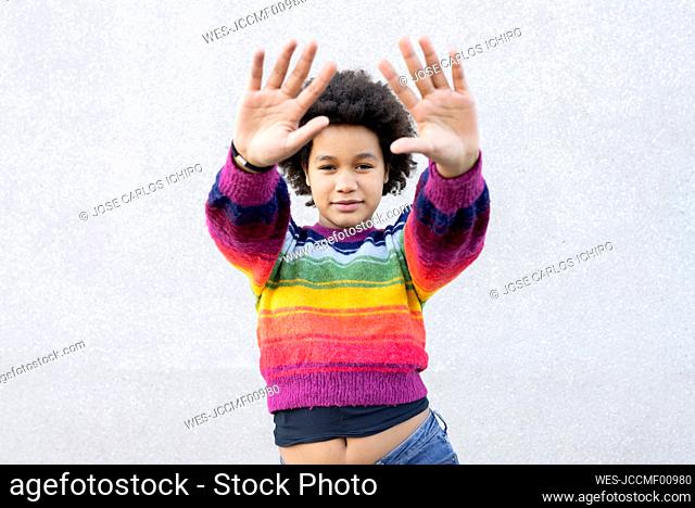 Girl with hand raised standing against gray wall