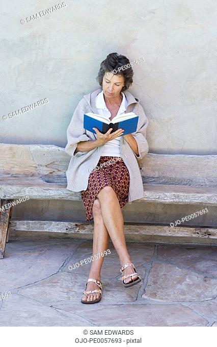 Woman sitting outdoors on wooden bench reading