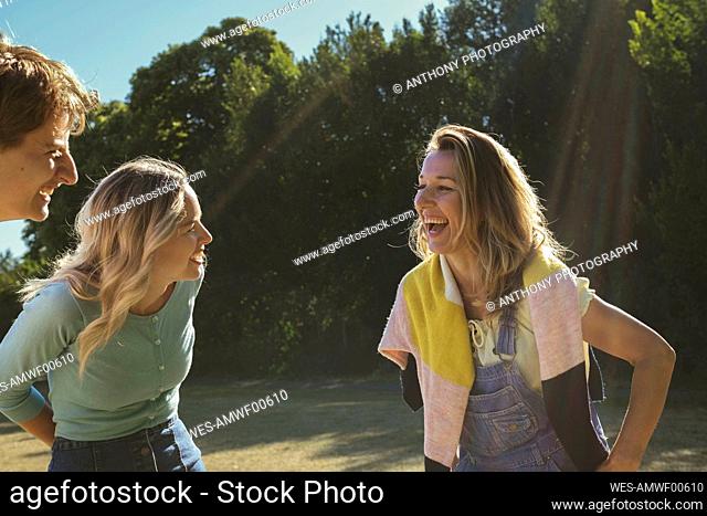 Cheerful woman having fun with friends at park on sunny day