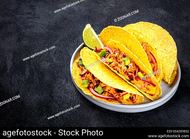 Cochinita pibil taco shells, a Mexican snack with pulled pork, avocado and marinated red onion, a close-up shot on a dark background with a place for text