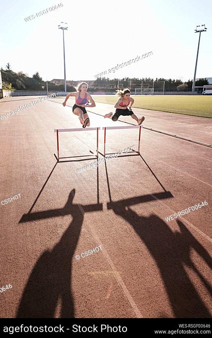 Young female athletes jumping over hurdle on training grounds