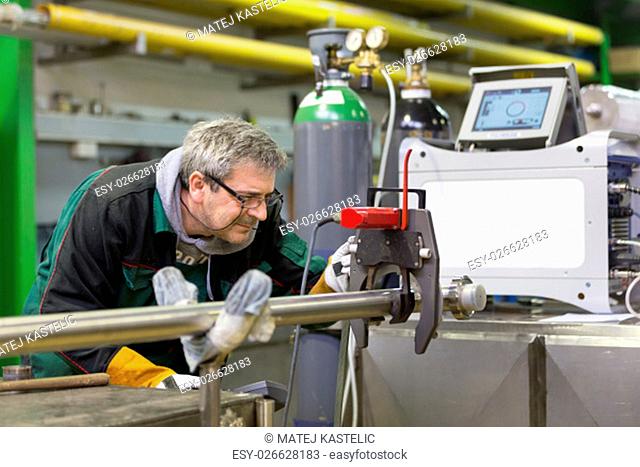 Industrial operator setting computer controlled process of orbital welding machine in stainless steel pipes manufacturing workshop