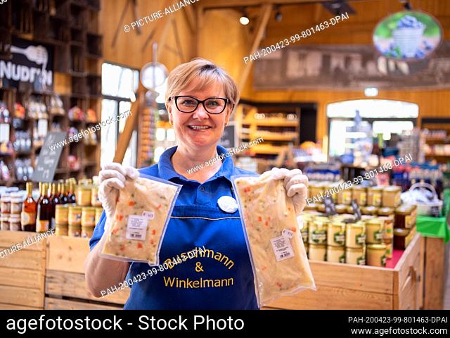 21 April 2020, Brandenburg, Beelitz/Gemeinde Klaistow: Saleswoman Iwona shows two packets of sous-vide pre-cooked chicken fricassee in the farm shop