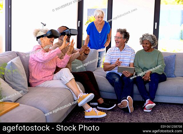 Multiracial seniors with digital pc looking at friends enjoying virtual reality simulator on sofa