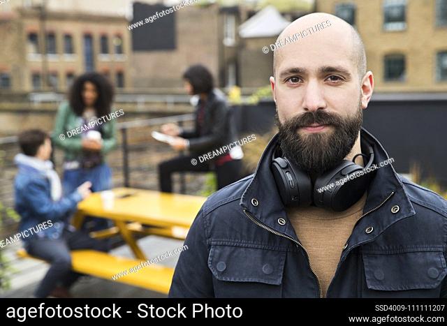 Portrait of man with group of friends working on tablets at outdoor patio table in co-working space in the background