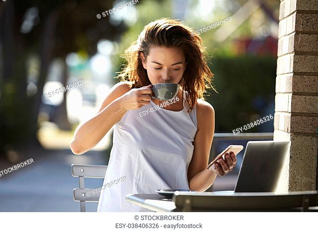 Woman using smartphone and laptop drinking coffee outside