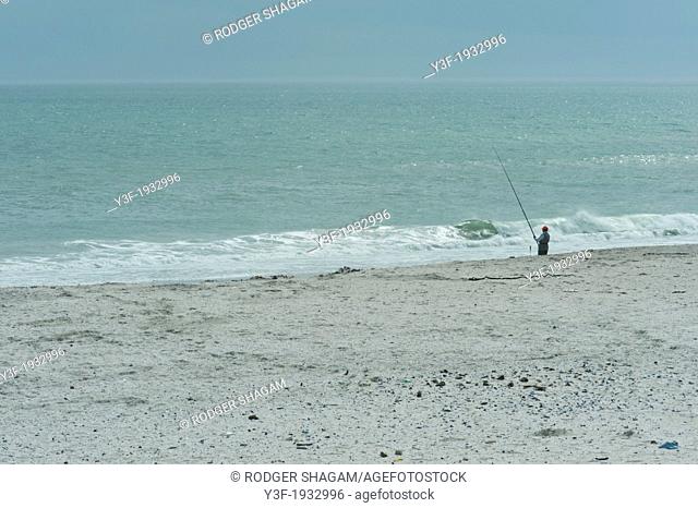 A lonely fisherman stands in solitude on a beach, line in the water, waiting ..