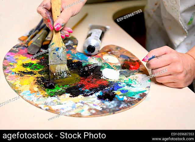 Creative female painter mixes palette of oil paints in palette. Close-up view. High quality photo