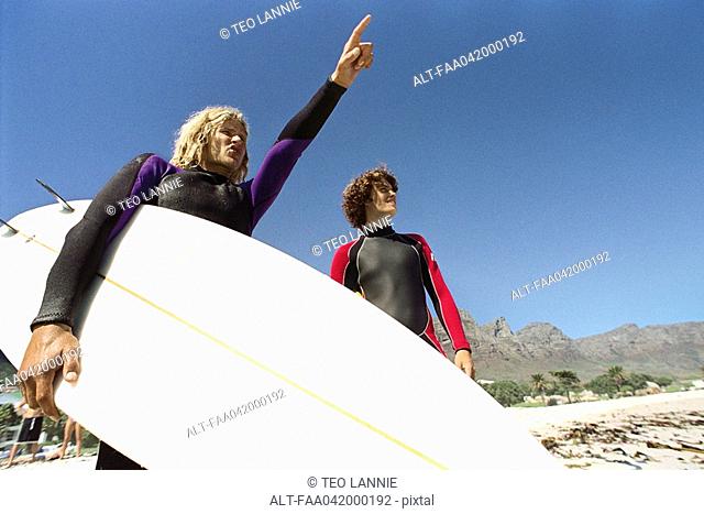 Surfers on beach, one pointing to distance