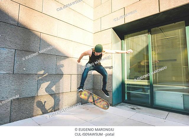 Young male urban skateboarder doing skateboarding jump trick in corner