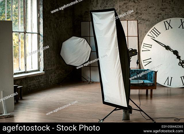 Photo studio with studio light and decorations. In the background is a huge clock with Roman numerals, there is a sofa. Studio with daylight