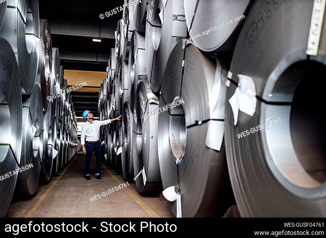 Businessman analyzing steel rolls while standing in industry