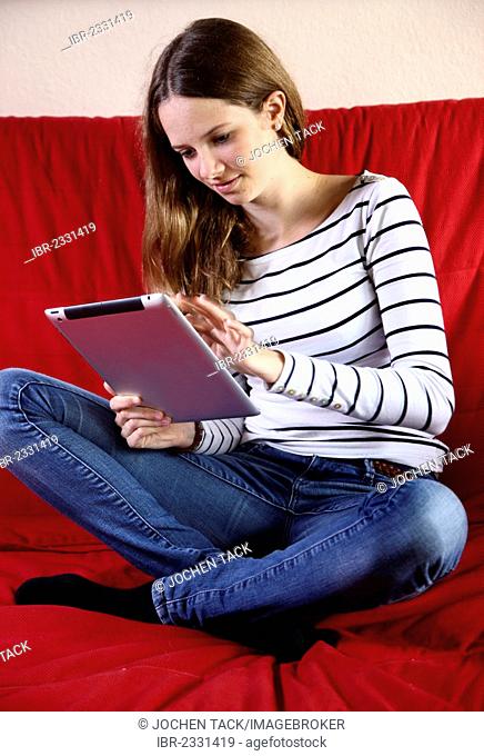 Girl sitting on a sofa holding an iPad, tablet computer with wireless internet access