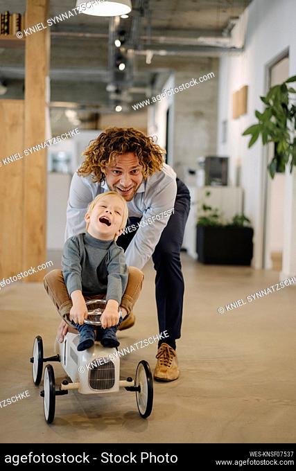 Businessman pushing son on toy car in office