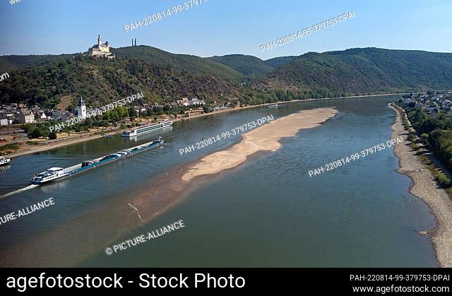 11 August 2022, Rhineland-Palatinate, Braubach: A cargo ship passes the sandbank at Braubach Grund at low tide. Marksburg Castle can be seen in the background