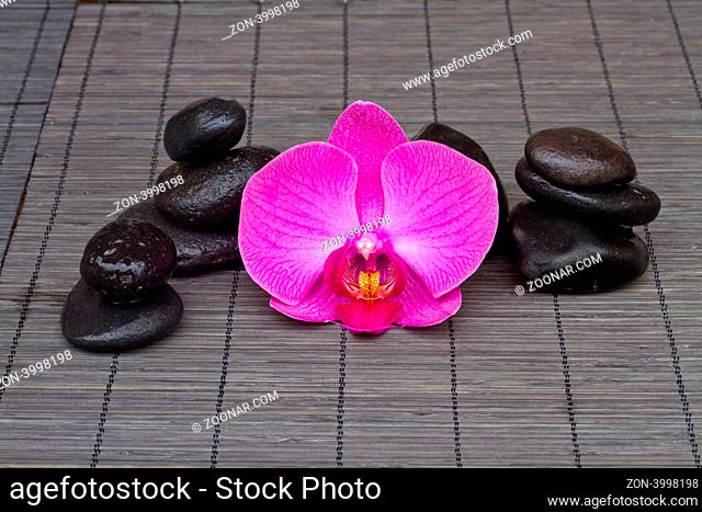 massage stones and orchid on black bamboo mat