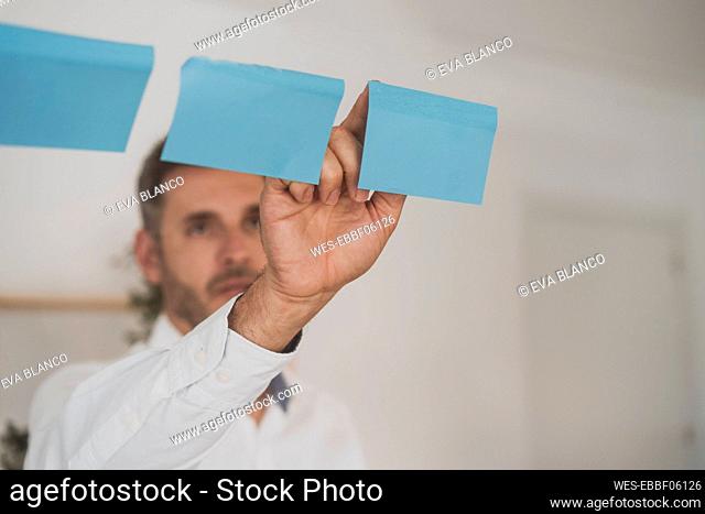 Businessman sticking blank adhesive note on glass