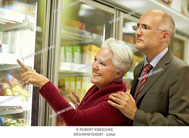 Germany, Cologne, Mature couple choosing from freezer in supermarket