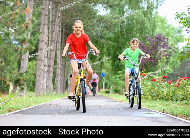 Two girls ride a bike on a bike path