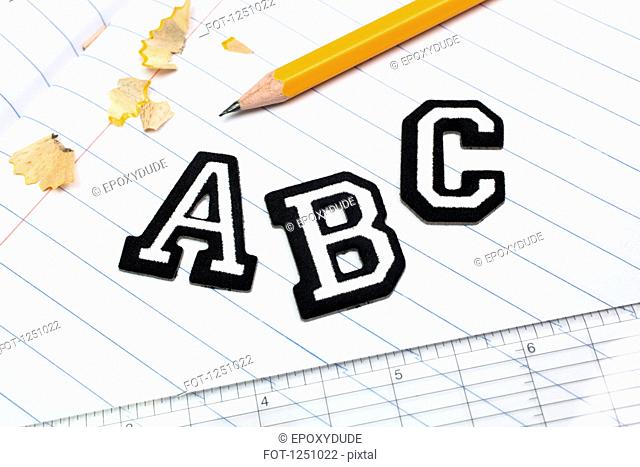 Varsity font stickers spelling out A, B, C atop a lined paper notebook with ruler and pencil