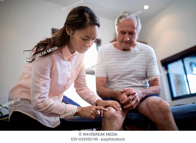 Low angle view of female therapist examining knee while male patient sitting on bed