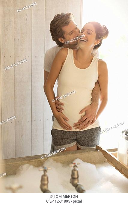 Laughing affectionate pregnant couple kissing preparing bubble bath