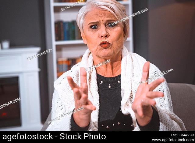 Caucasian Woman Of Retirement Age Feels Anger. She Gestures Violently With Her Hands, Grimacing, Tightened Her Lips From Anger