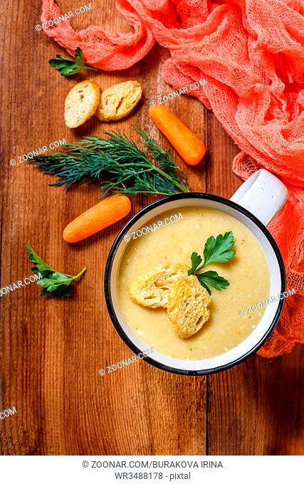 Vegetable soup puree with cheese in a white mug and vegetables in the background