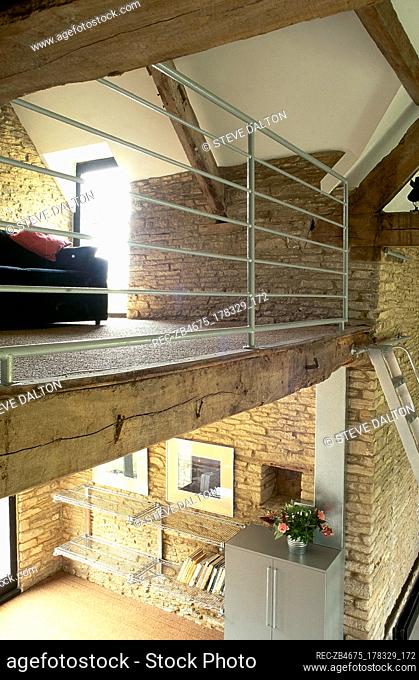 View of the upper and lower levels of a converted stone barn with exposed roof trusses, steel balcony railing, and metal bookshelves