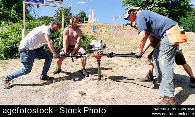 PRODUCTION - 14 June 2023, Schleswig-Holstein, Kiel: Woodworkers drill a hole in the sand at the ""Kinder-Spiellinie"" play area during preparatory work for...