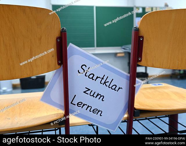PRODUCTION - 29 August 2023, Hesse, Wiesbaden: A laminated sheet of paper with the inscription ""Ready to learn"" is placed between two chairs in the classroom...
