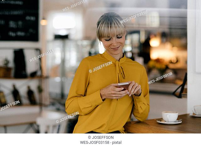 Blond businesswoman using smartphone in a coffee shop, reading text messages