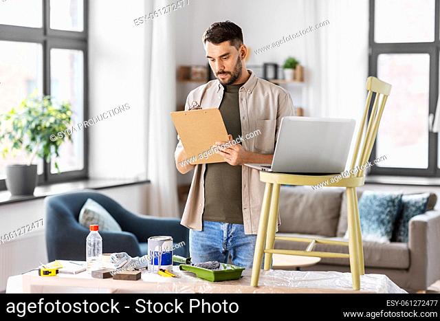 man with clipboard and laptop renovating old chair