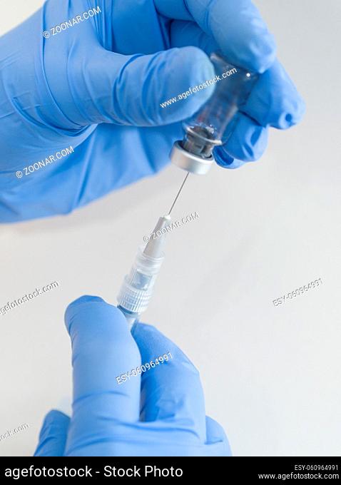 Hands in Blue Rubber Gloves Holding Medical Syringe and Vial Closeup on White Background