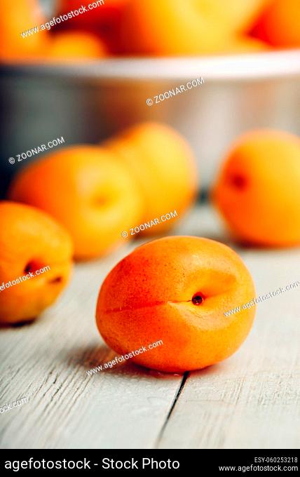 Mellow apricots over light wooden surface and metal bowl with fruits on background
