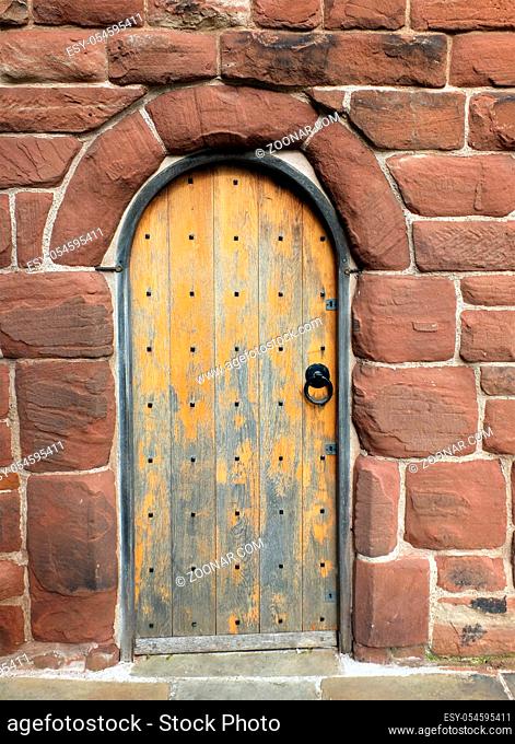 an ancient brown wooden door in a red sandstone medieval wall