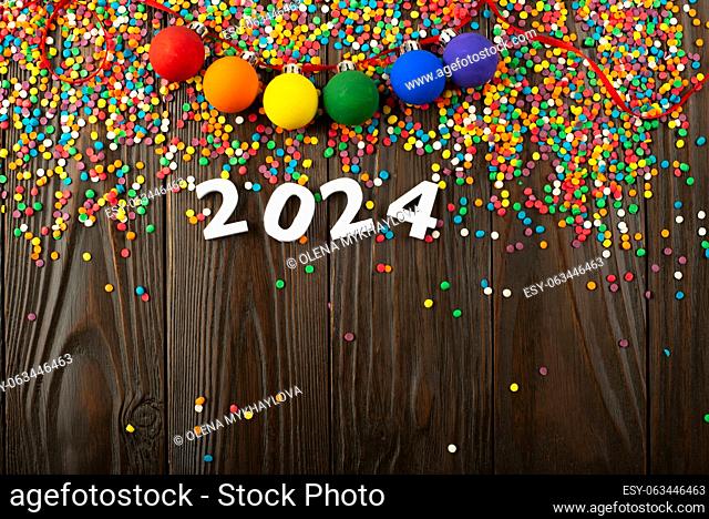 White numbers 2024 and color sugar sprinkles on wooden table with color balls garland
