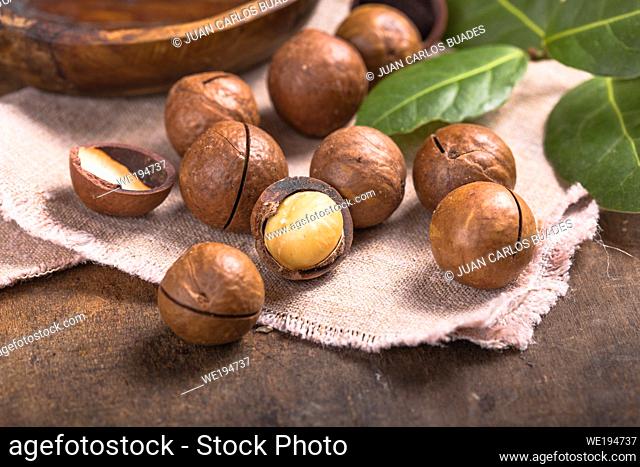 Pile macadamia nuts open kernels and shells in burlap bag on wooden background