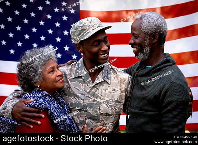 Portrait of a young adult African American male soldier embracing with his parents and smiling to each other in front of a US flag