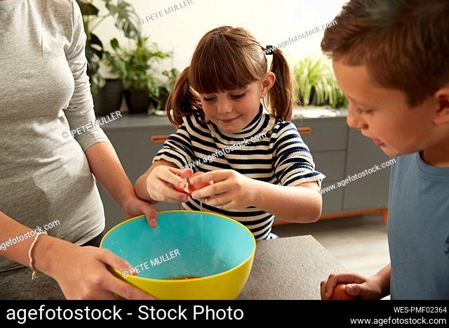 Smiling girl helping sister in preparing cookies by brother at home