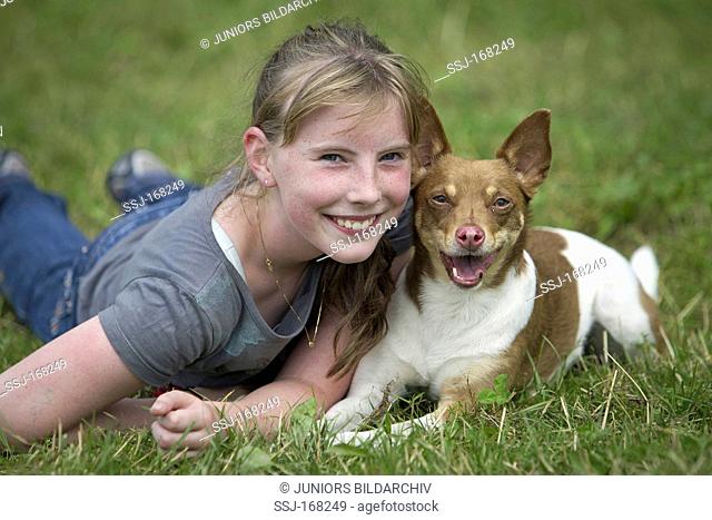 Basenji. Girl lying with Basenji-mix on a meadow with both smiling into the camera