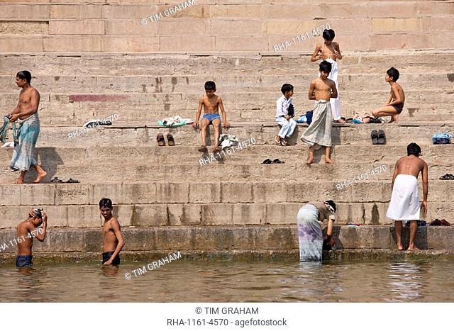 Indian Hindu pilgrims men and boys bathing in The Ganges River by steps of the Ghats in Holy City of Varanasi, Benares, India
