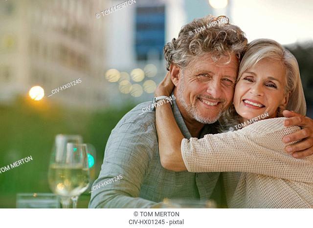 Portrait smiling senior couple hugging at urban sidewalk cafe