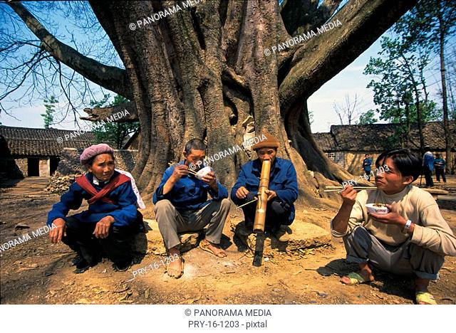 Buyi people squatting, eating beside tree