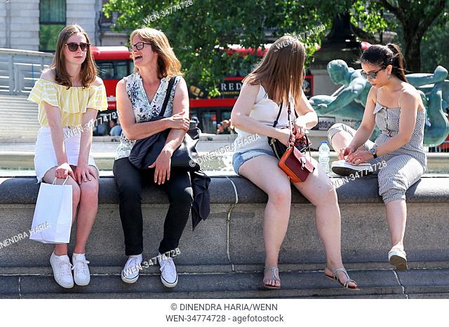 Londoners and tourists sitting on the edge of the fountain in Trafalgar Square on another hot and humid day in the capital